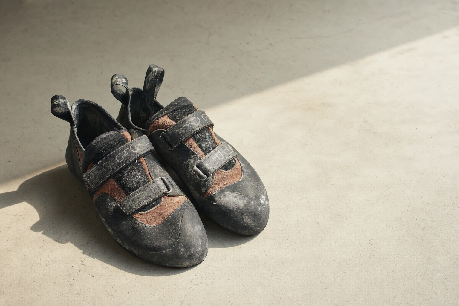 A worn, chalk-dusted pair of climbing shoes resting on a warm concrete surface in soft natural light.